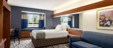 Une chambre d’hôtel avec un lit, un bureau, une chaise, un canapé et une grande fenêtre avec des rideaux.