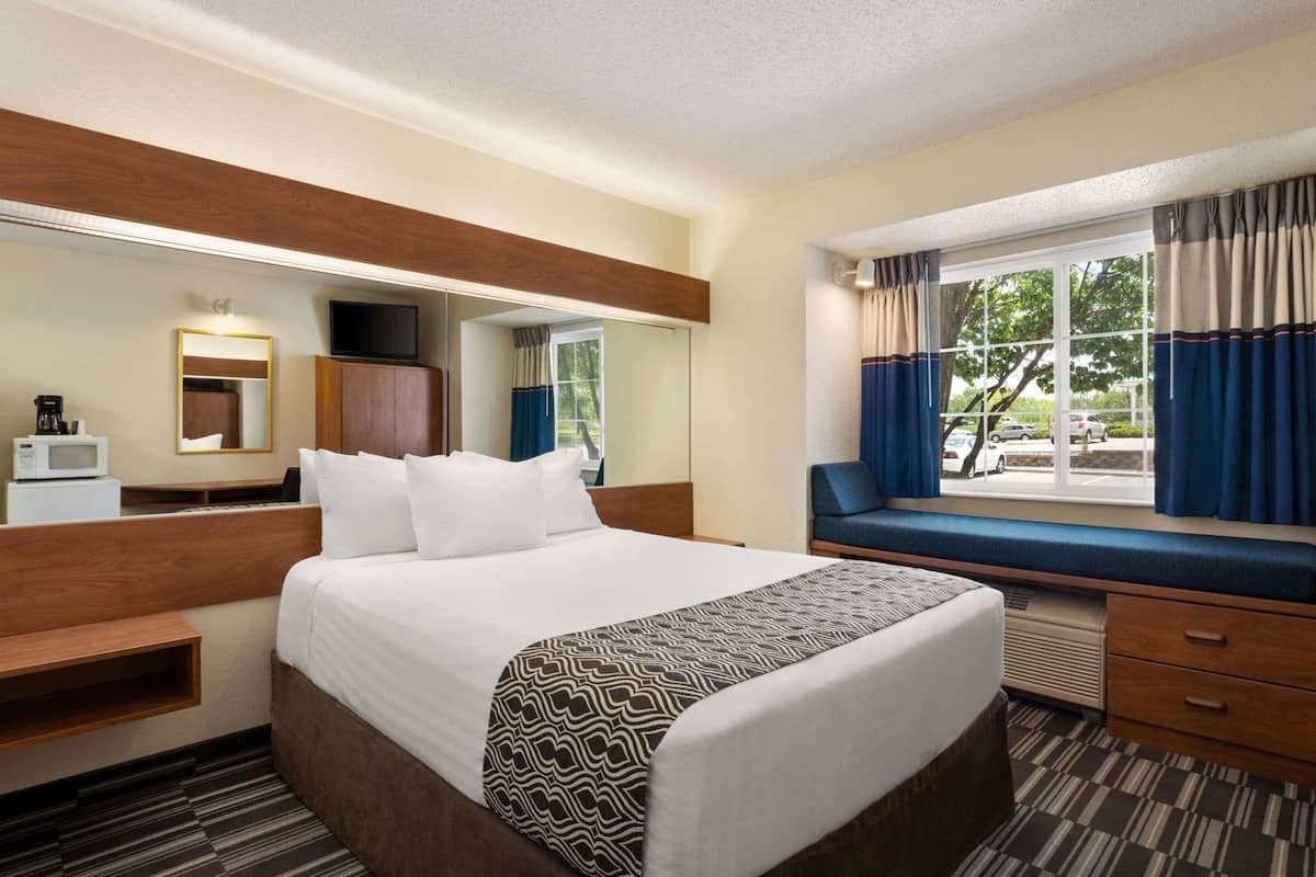 A hotel room with a bed, a desk, a chair, a window with curtains, and a view of the outside.