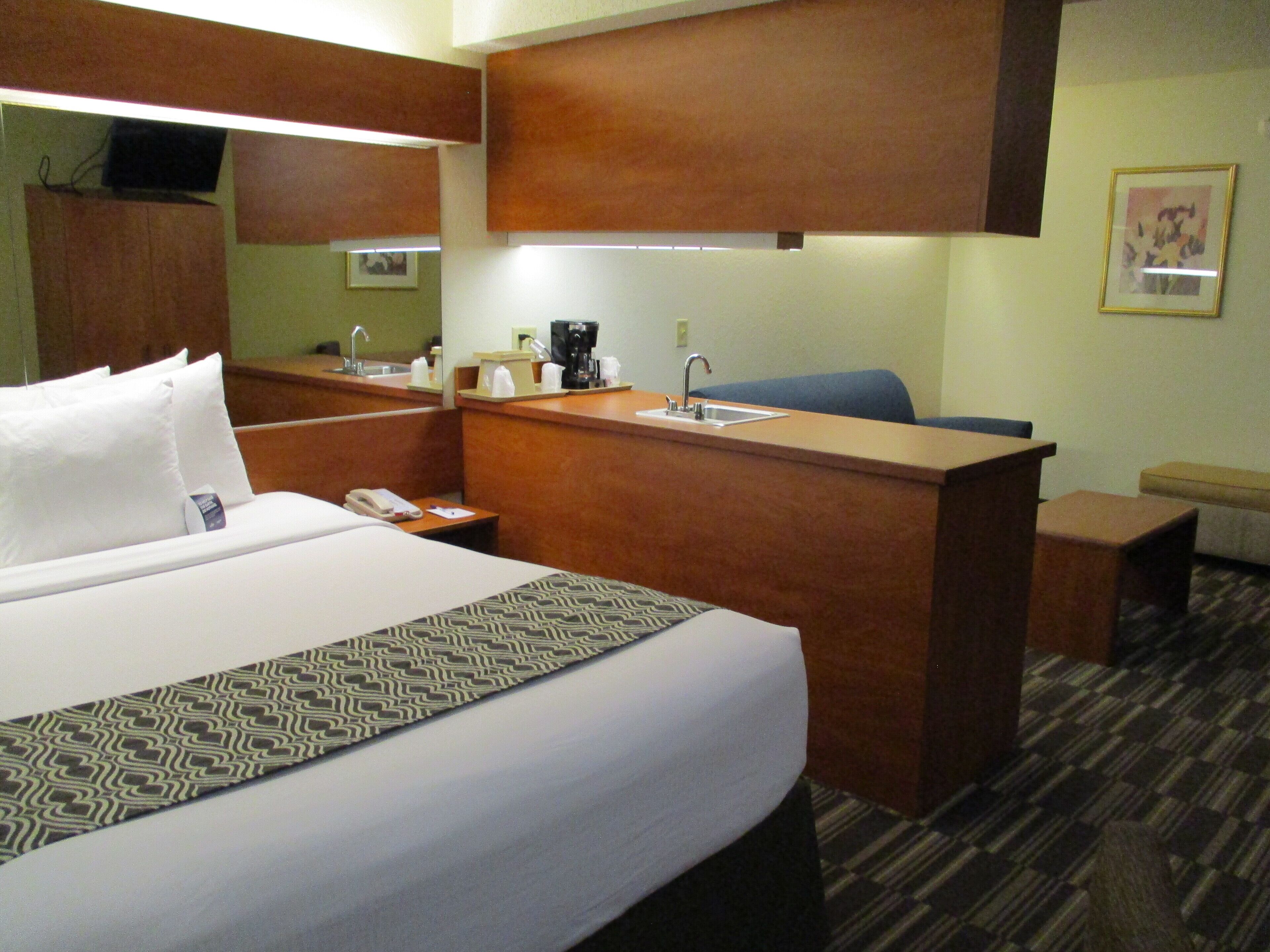 Una habitación de hotel con cama, escritorio, silla, cafetera y teléfono.