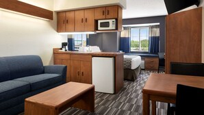 Habitación de hotel compacta con kitchenette, sofá, mesa de comedor y refrigerador pequeño.