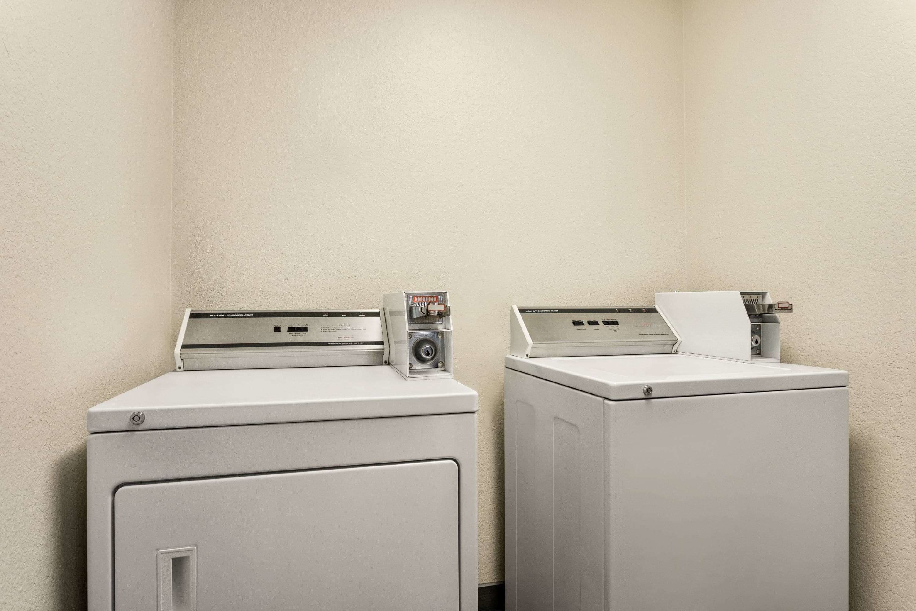 Two front-loading washing machines in a corner with a plain wall.