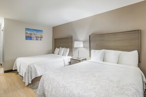 Habitación de hotel con dos camas, una mesita de noche con lámpara, un cuadro en la pared y suelo de madera.
