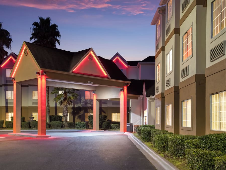 A hotel entrance with a covered walkway, palm trees, and a clear sky.
