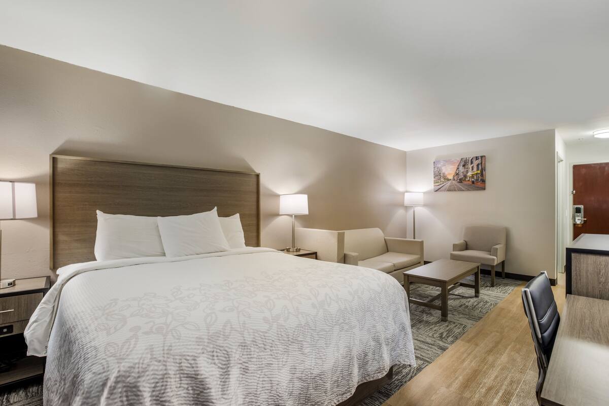 A hotel room with a large bed, two armchairs, a small table, and a desk.