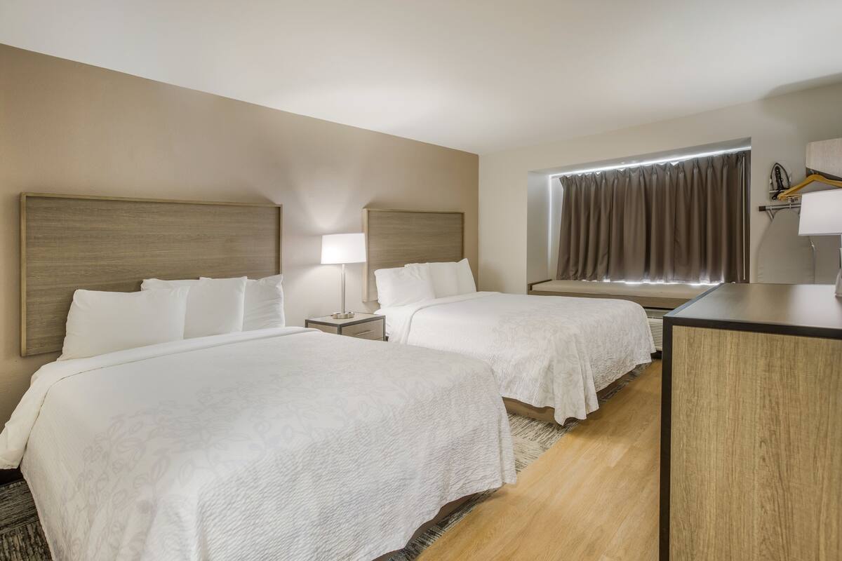 A hotel room with two beds, a desk, a lamp, and a window with curtains.