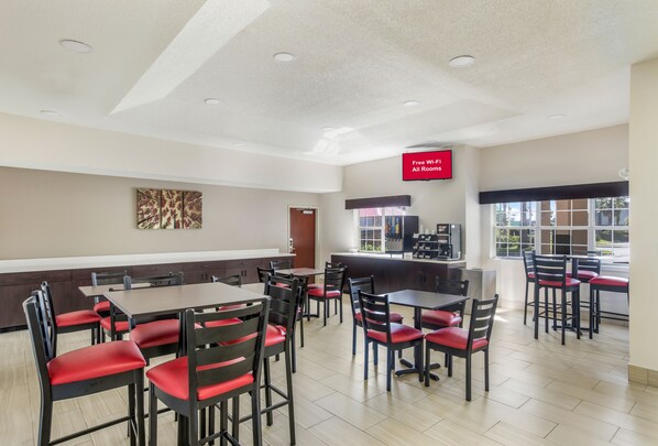 A spacious dining area with multiple tables and chairs, a kitchen counter, and a sign indicating free Wi-Fi availability. - Red Roof Inn PLUS+ & Suites Savannah - I-95 (Savannah)
