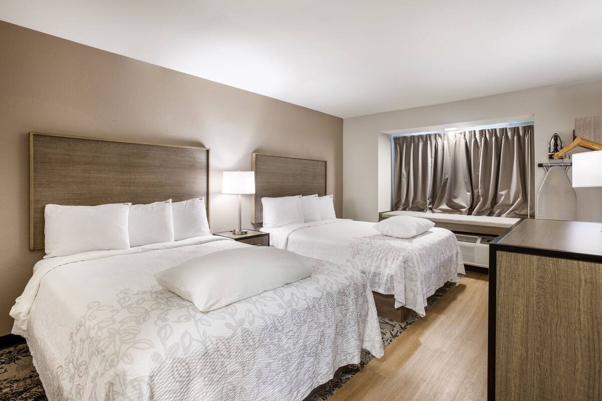 A hotel room with two beds, a desk, and a window with curtains.