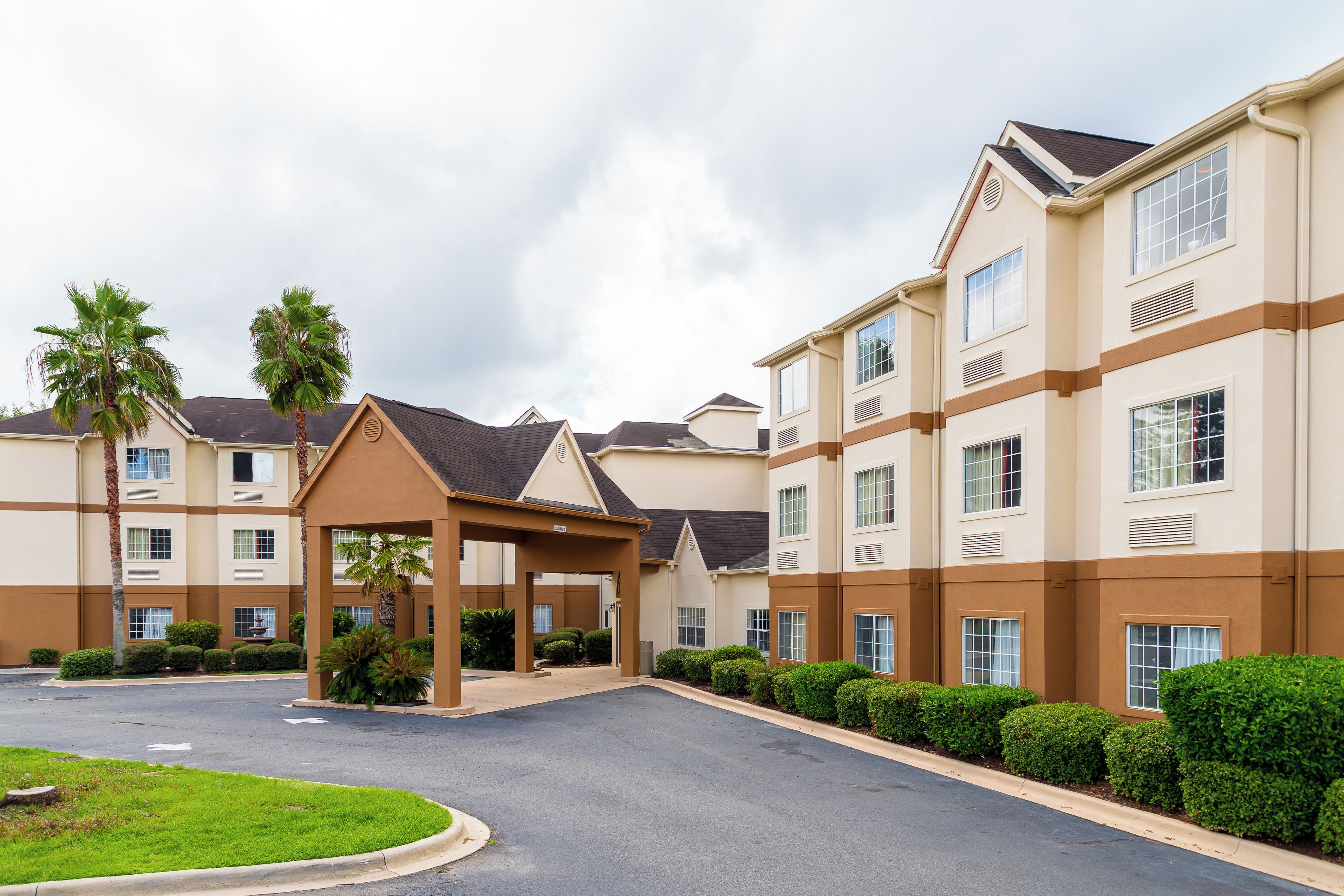 A multi-story hotel with a covered entrance, palm trees, and a well-maintained lawn.