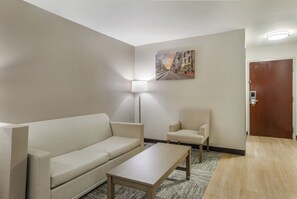 A hotel room with a sofa, armchair, and a small table. There is a painting on the wall and a door with a lock.