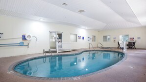 An indoor swimming pool with a clear water surface, surrounded by a tiled floor and walls. There are signs on the walls, a white railing around the pool, and a door leading to another room. - Red Roof Inn PLUS+ & Suites Savannah - I-95 (Savannah)