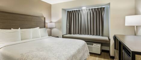 Habitación de hotel con una cama grande, lámparas de noche, una ventana con cortinas, un escritorio y un calefactor incorporado.