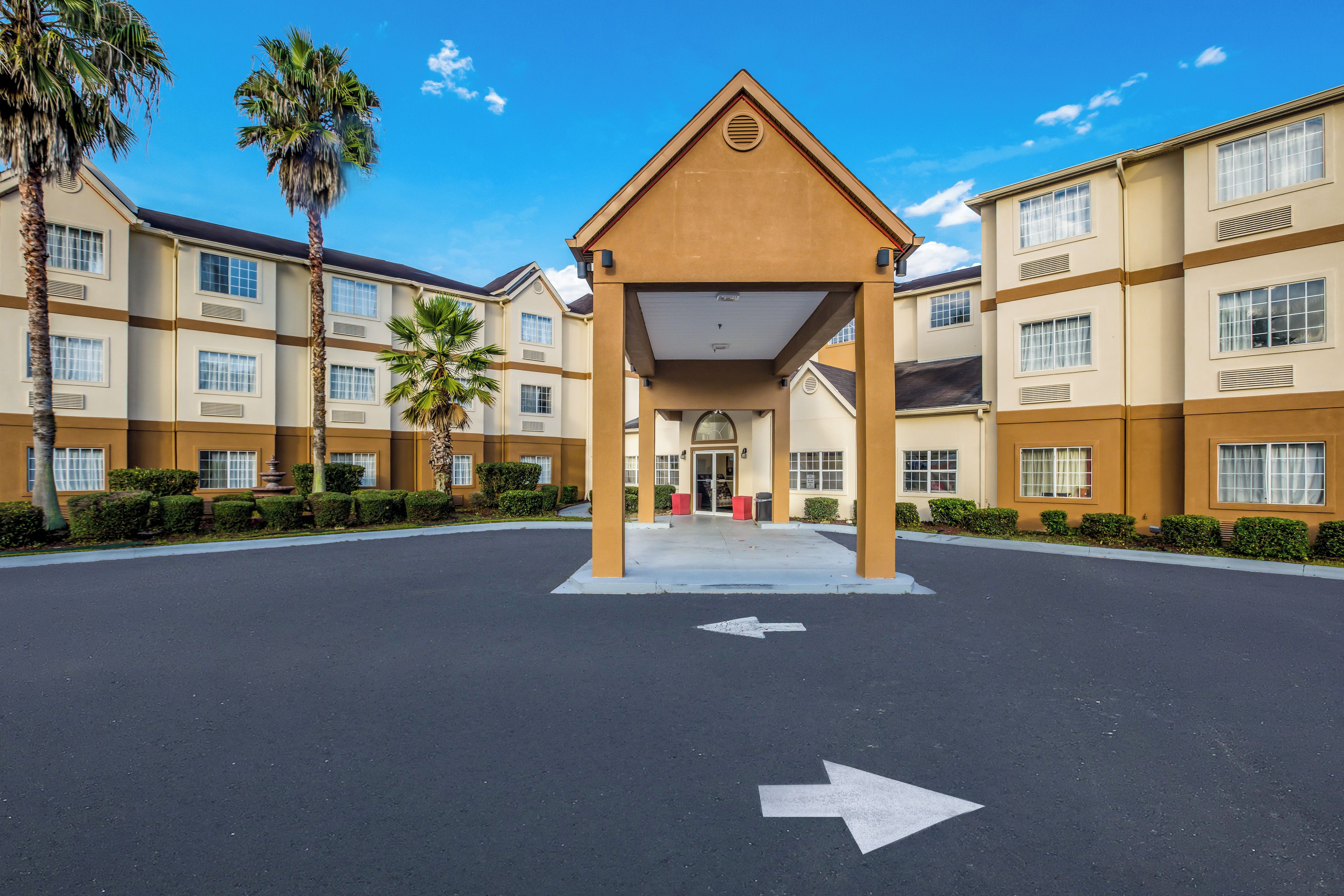 A hotel entrance with a covered waiting area, palm trees, and a clear sky.
