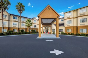 A hotel entrance with a covered waiting area, palm trees, and a clear sky. - Red Roof Inn PLUS+ & Suites Savannah - I-95 (Savannah)
