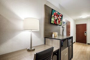 Habitación de hotel con escritorio, silla, lámpara, televisión y minibar.