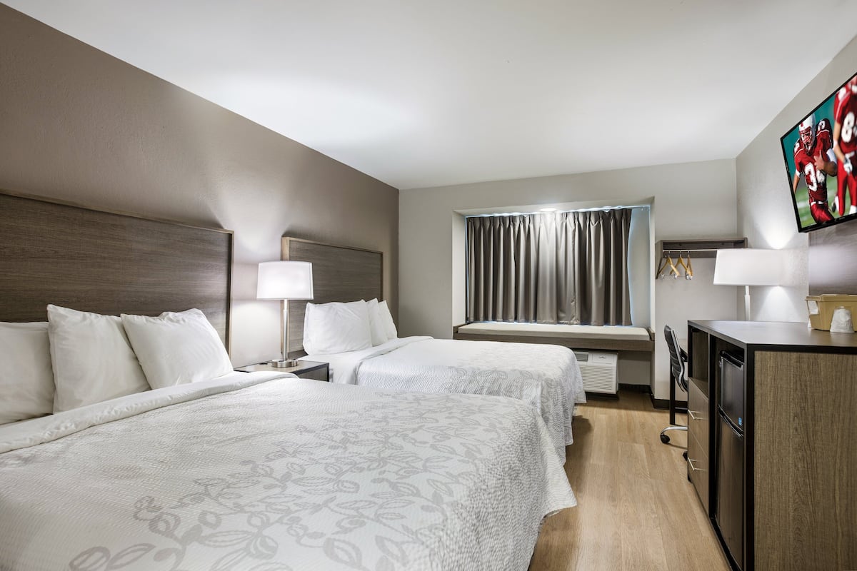Habitación de hotel con dos camas, un escritorio, un televisor y una ventana con cortinas.