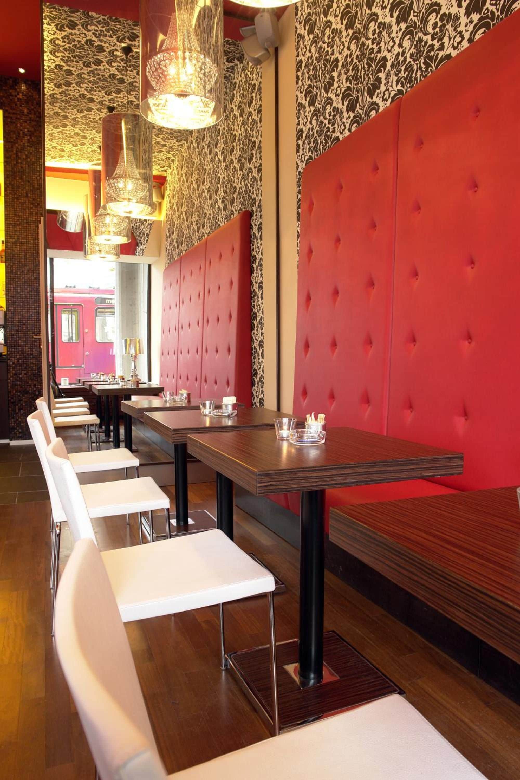Interior de restaurante con una barra larga, sillas blancas y asientos tapizados en rojo.