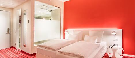 A modern hotel room with a red carpet, a white bed, and a red accent wall.