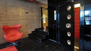 Un hall d’entrée moderne avec un fauteuil rouge, un escalier et un ascenseur noir agrémenté d’éléments décoratifs rouges.