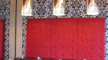 Un restaurante con asientos tapizados en rojo, mesas redondas y un papel pintado decorado.