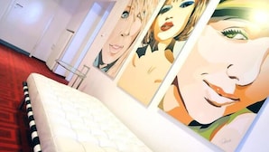 Une chambre d’hôtel avec un lit blanc, une moquette rouge et trois grands tableaux accrochés au mur.
