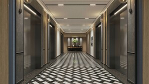 Un couloir moderne avec un sol à carreaux, des ascenseurs et un éclairage encastré.