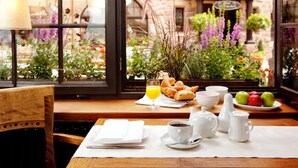 Ein Frühstückstisch mit Croissants, einem Orangensaftglas und Blick auf einen Garten mit Blumen und einem Steinhaus.