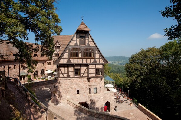 A historic building with a prominent tower, a courtyard with outdoor seating, and a scenic view of the surrounding landscape.