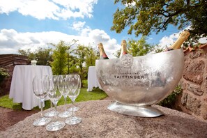 Un cubo plateado para champán con la etiqueta "Taittinger", dos botellas de champán y cuatro copas de vino vacías sobre una superficie de piedra.