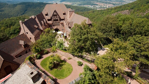 Ein großes, historisches Gebäude mit einem von Bäumen umgebenen Innenhof, gelegen in einer gebirgigen Landschaft.