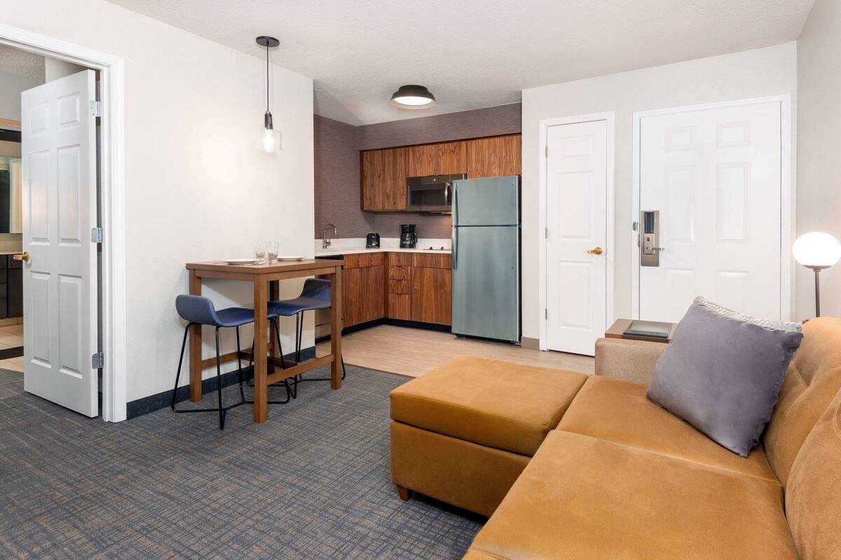 Een ruimtelijk ingerichte leefruimte met kitchenette, een bank, een eethoek en een deur naar een andere kamer.