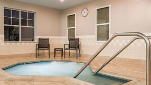 Una piscina con una escalera metálica, dos sillas y un reloj en la pared.