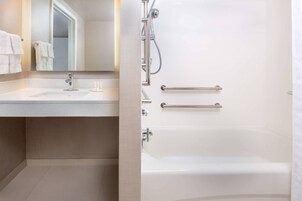 Un baño moderno con lavamanos, espejo y bañera blancos.
