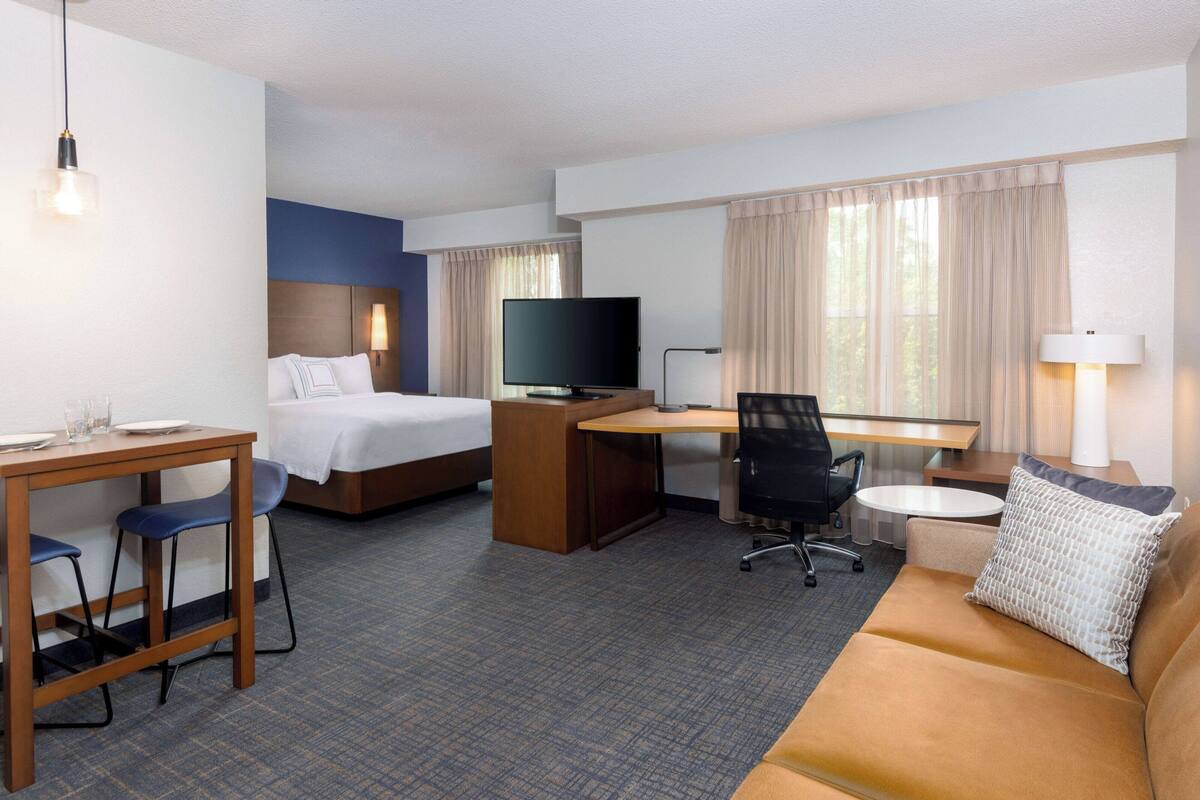 Een hotelkamer met een bed, een bureau met een computer, een televisie, een bank en een zithoek met stoelen en een tafel.