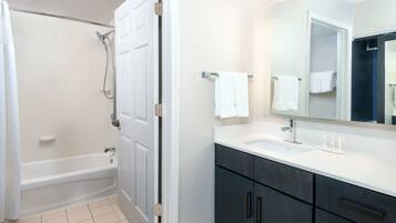 A bathroom with a bathtub, a sink, dark cabinets, and a mirror.