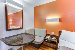 Une chambre d’hôtel avec une table en bois, un banc rembourré, un lit et un téléphone fixé au mur.