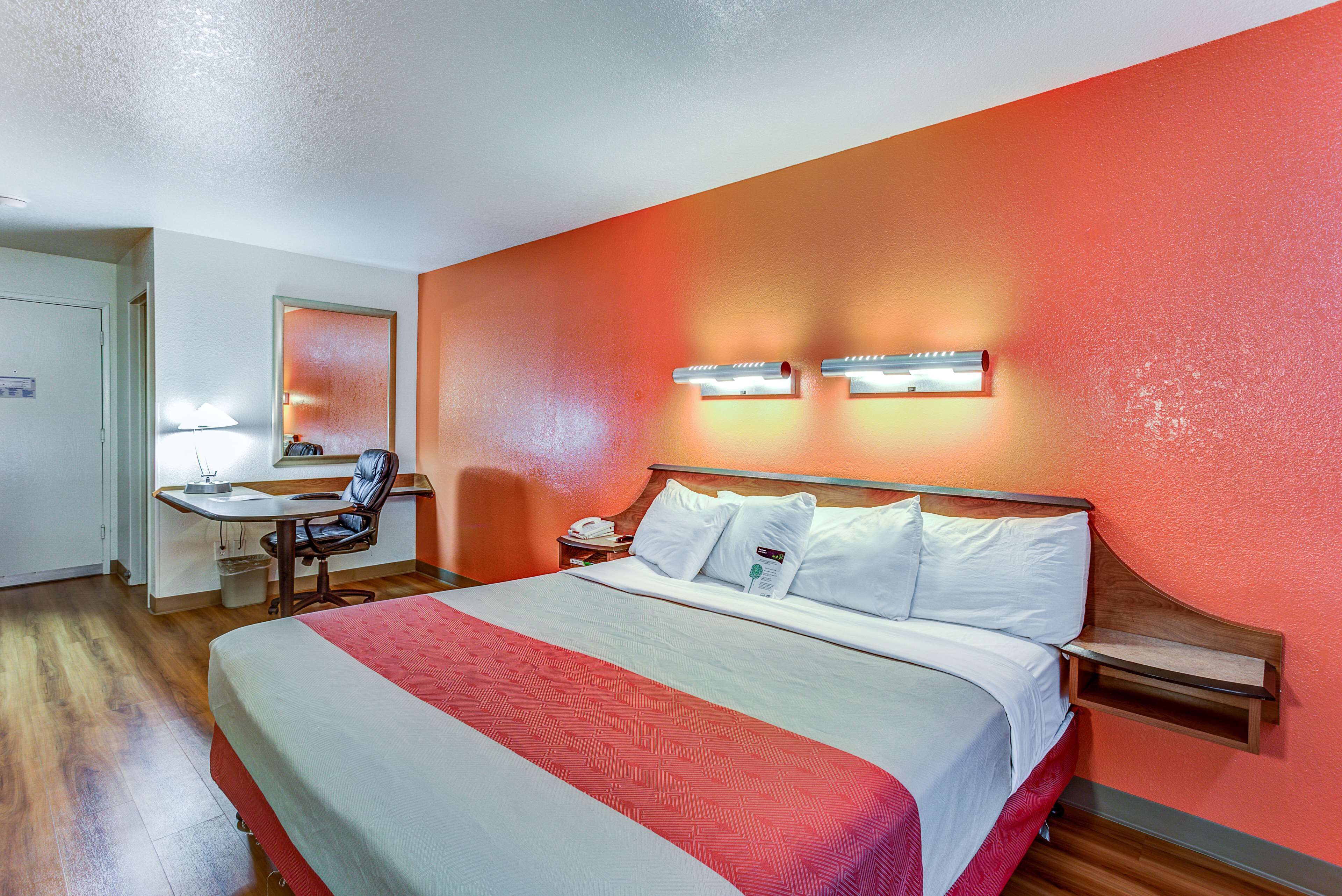 Habitación de hotel con cama, escritorio, silla y mesita de noche con lámpara.