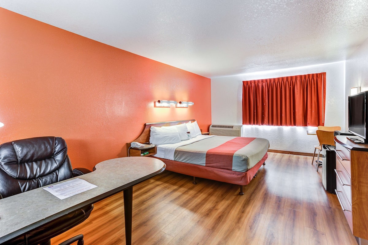 A hotel room with a bed, a desk, a chair, a TV, and a window with curtains.