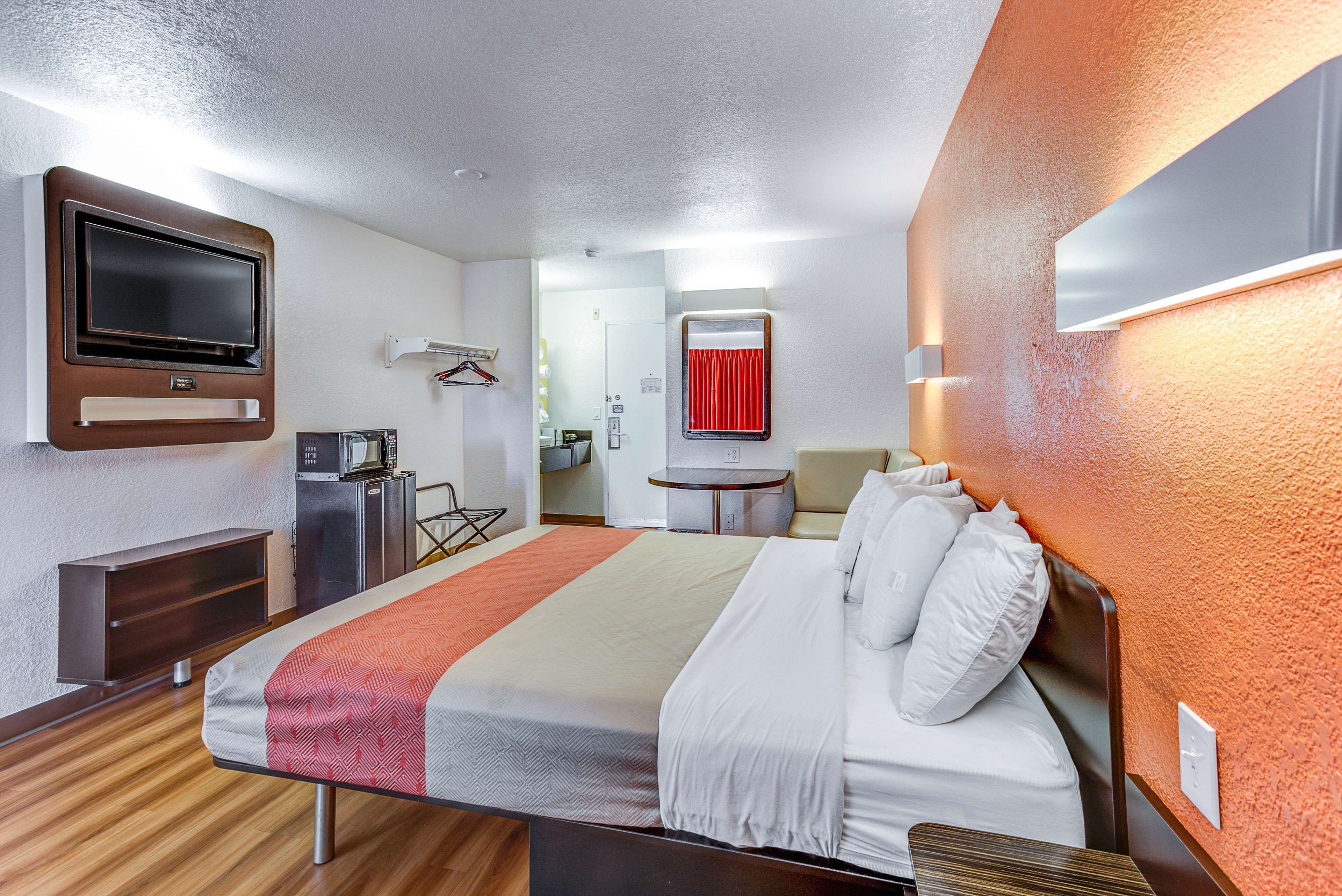 Habitación de hotel con cama, escritorio, televisión, minibar y baño visible a través de una puerta abierta.