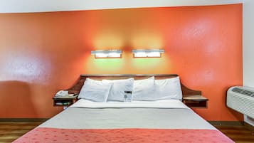 Une chambre d’hôtel comprenant un lit, deux tables de chevet, une petite table, un radiateur fixé au mur et un mur muni de deux luminaires.