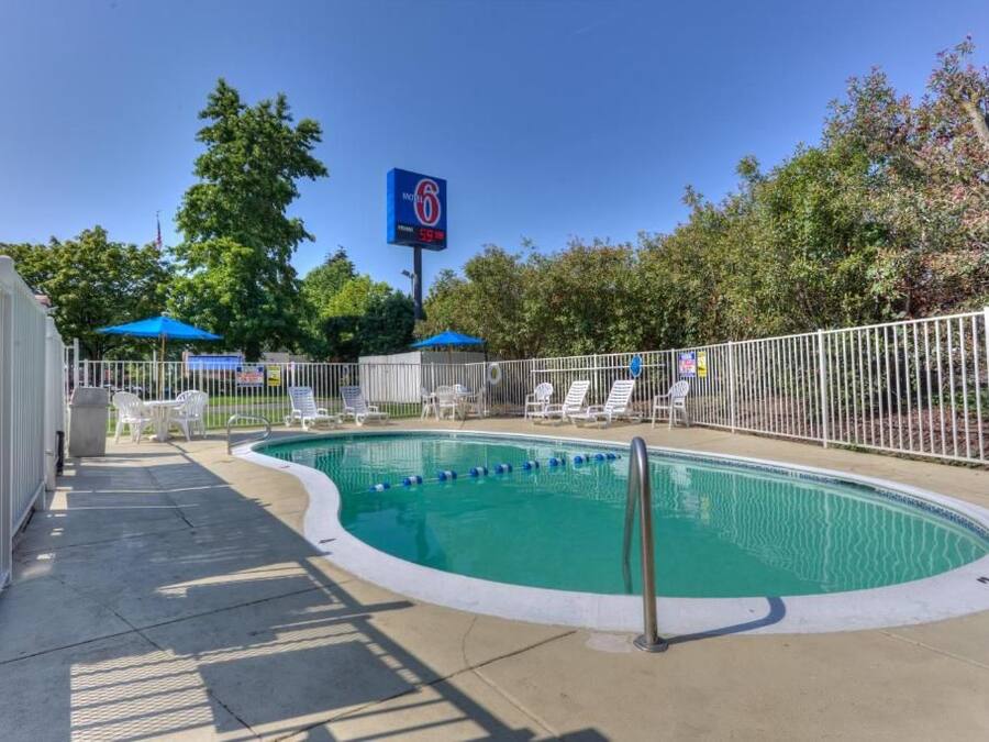 A swimming pool with a white fence, lounge chairs, and a blue umbrella.