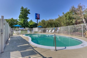 Una piscina con cerco blanco, sillas de descanso y una sombrilla azul.