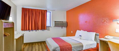 Quarto de hotel com cama, escrivaninha, cadeira, televisão e ar condicionado.