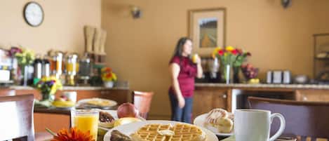 A breakfast table with waffles, a muffin, a glass of orange juice, and a flower.