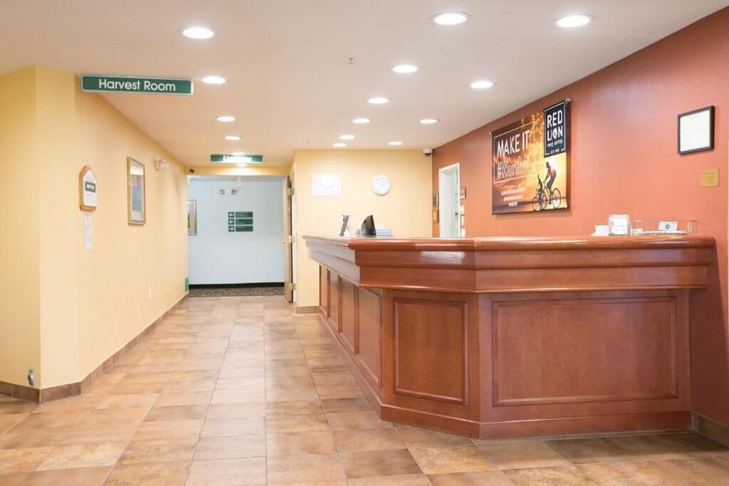 A hotel reception area with a wooden reception desk, a sign for the Harvest Room, and a Red Lion sign on the wall.
