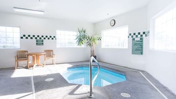 Zona de piscina con una pequeña piscina, dos sillas de madera, una planta en maceta y un reloj en la pared.