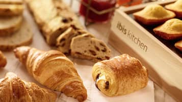 Diversas opciones de panadería, incluyendo croissants y pan, sobre una bandeja de madera con la etiqueta 'Ibis Kitchen' y un recipiente de vidrio con mermelada.