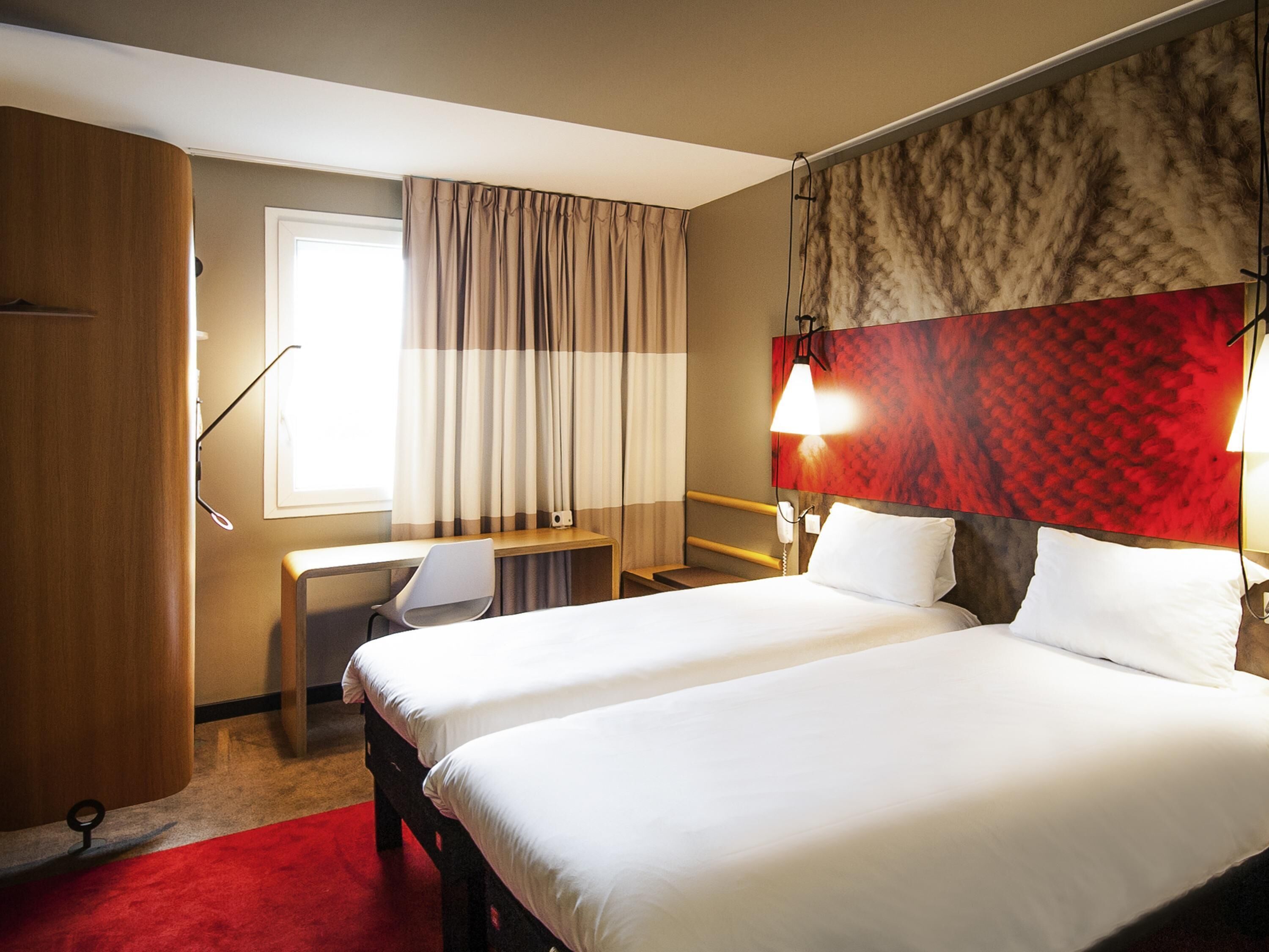 A hotel room with two beds, a desk, a chair, a telephone, and a window with curtains.