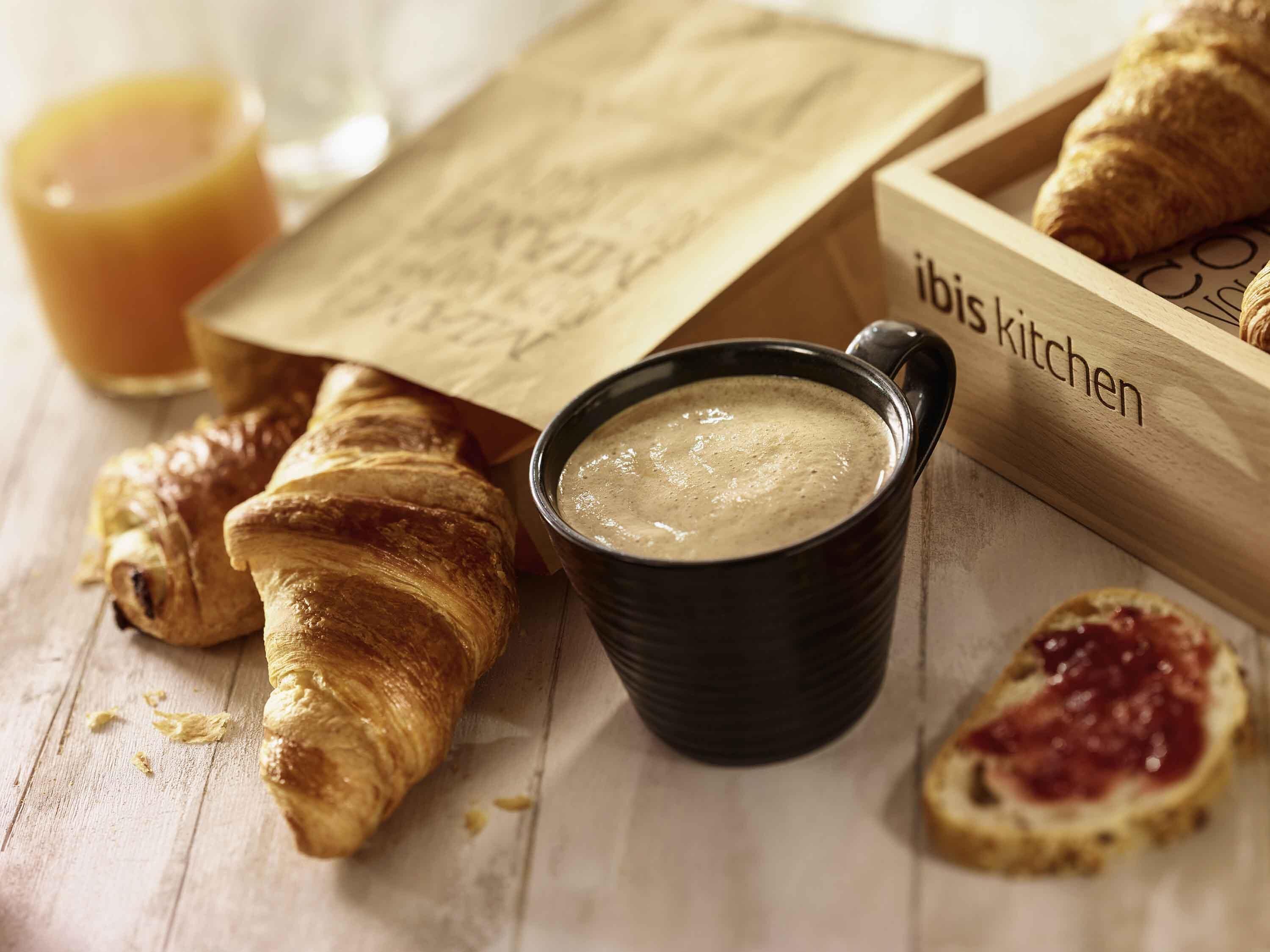 A wooden tray with croissants, a bowl of soup, and a glass of orange juice.
