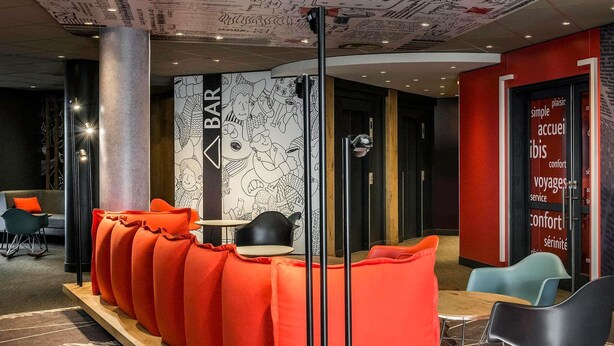A modern bar area with a long bench, black chairs, and a red accent wall.