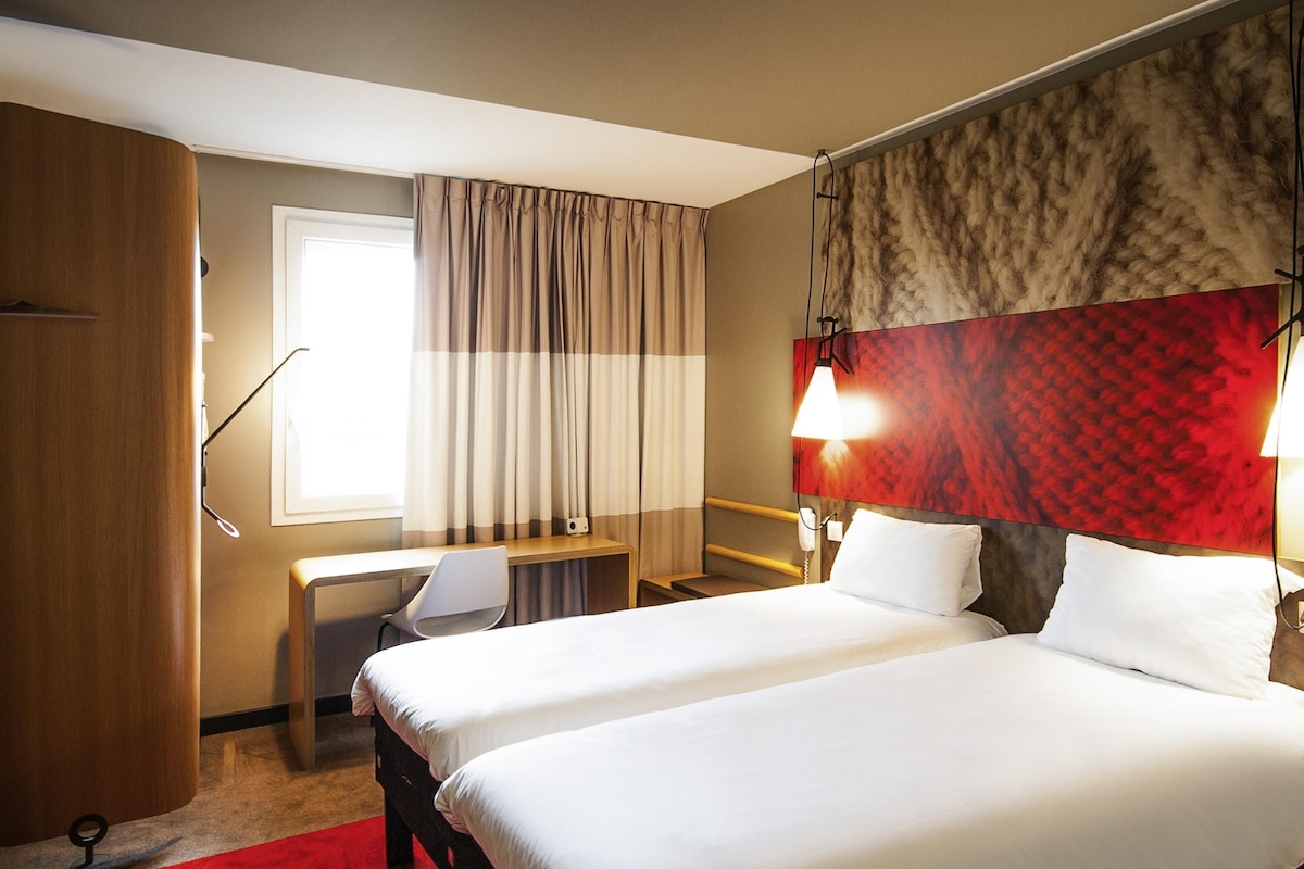 A hotel room with two beds, a desk, a chair, a telephone, and a window with curtains.